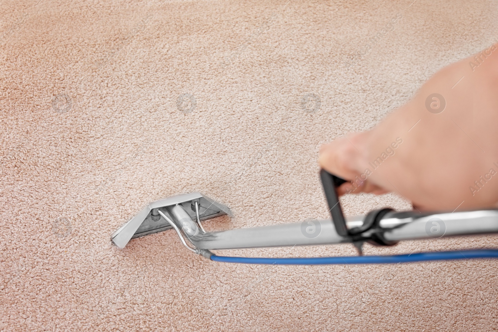 Photo of Male worker removing dirt from carpet with professional vacuum cleaner indoors