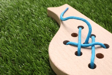 Photo of Wooden whale figure with holes and lace on artificial grass, closeup and space for text. Educational toy for motor skills development