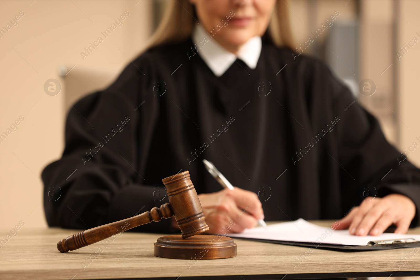 Photo of Judge working with document indoors, selective focus. Wooden mallet on table