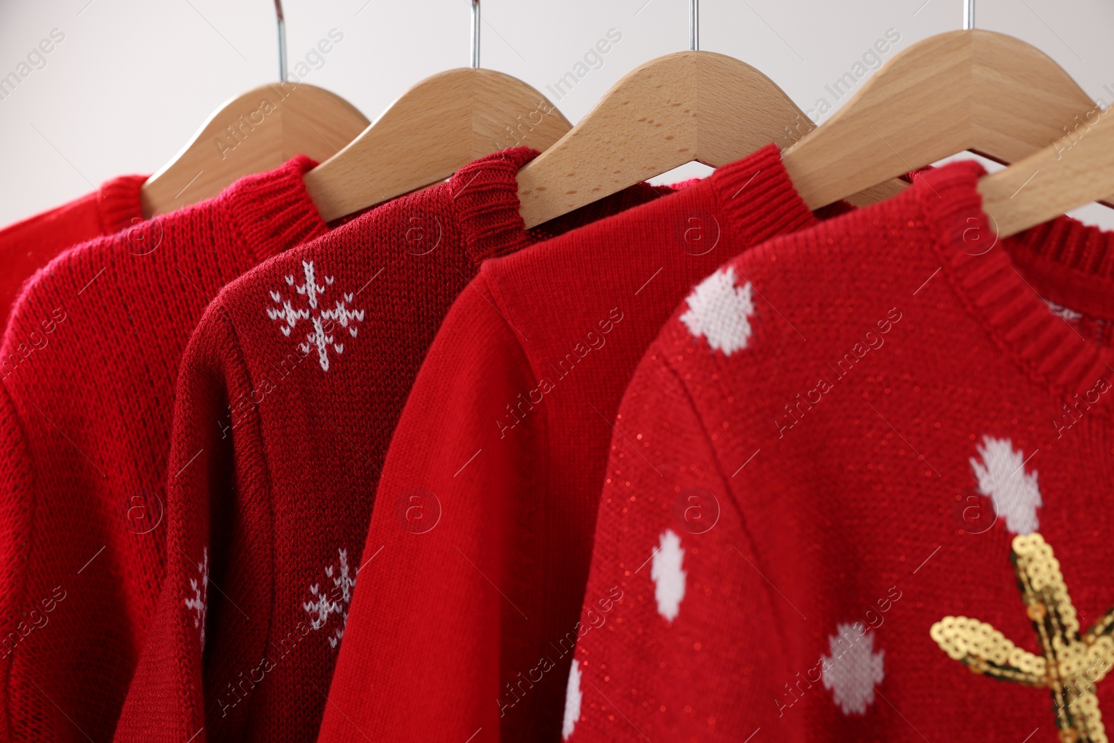 Photo of Different Christmas sweaters hanging on rack against light background, closeup