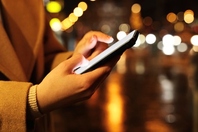 Woman using smartphone on night city street, closeup. Space for text