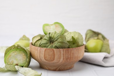 Photo of Fresh green tomatillos with husk in bowl on white tiled table, closeup