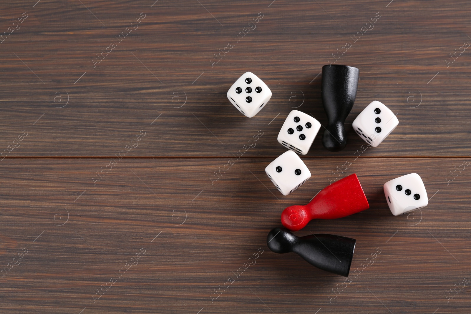 Photo of Many white dices and color game pieces on wooden table, flat lay. Space for text