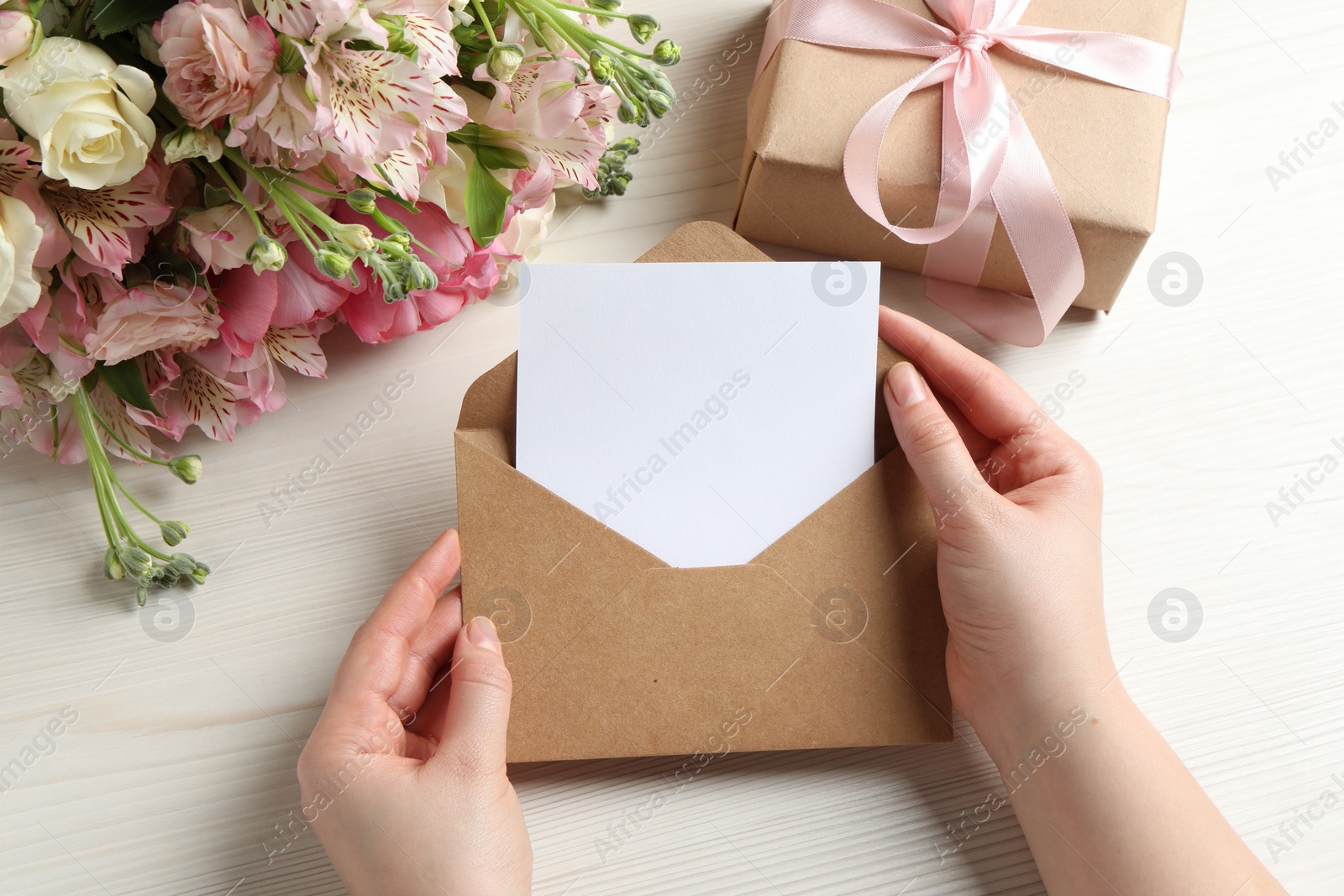 Photo of Happy Mother's Day. Woman holding envelope with blank card at white wooden table, top view