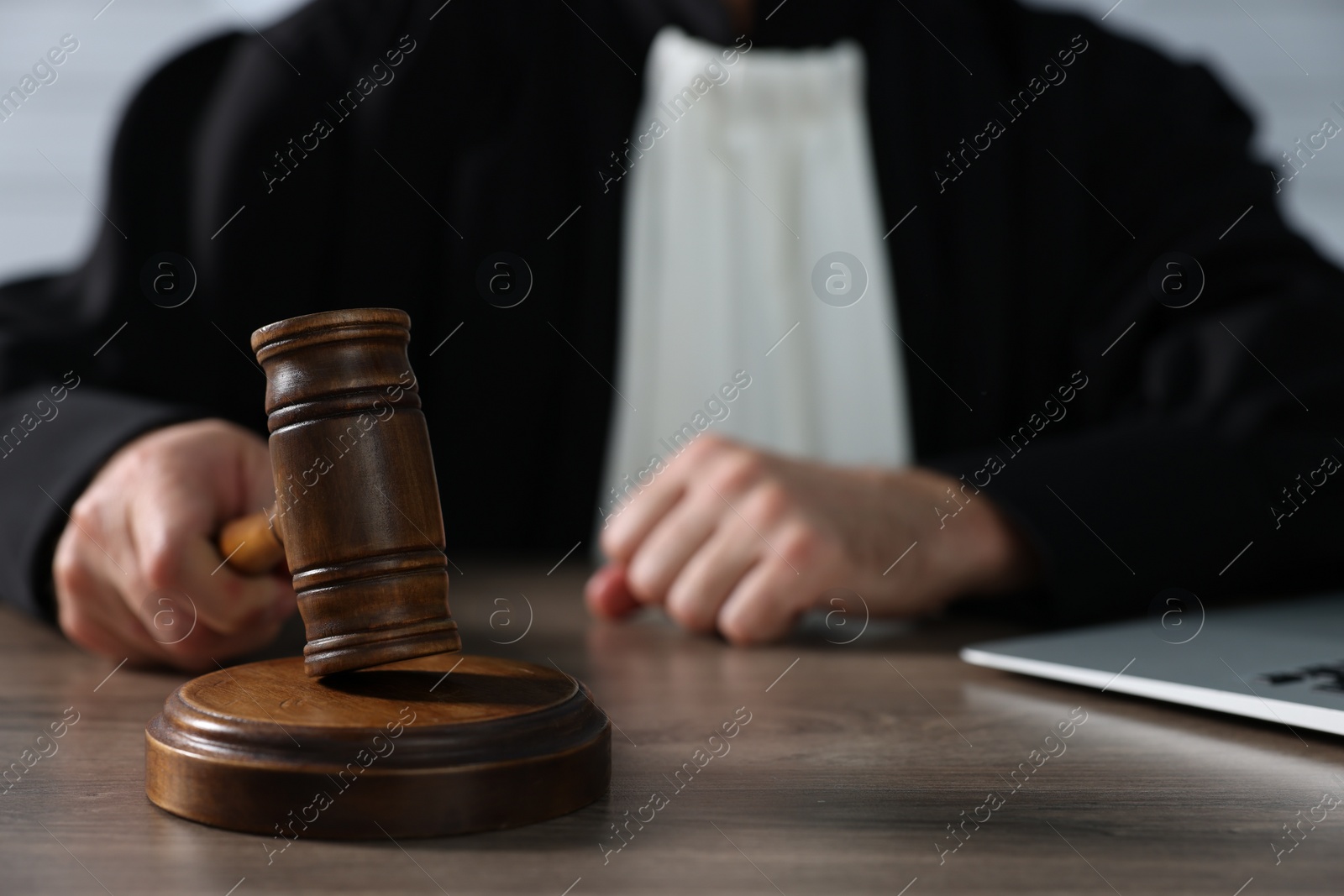 Photo of Judge with gavel and laptop sitting at wooden table, closeup