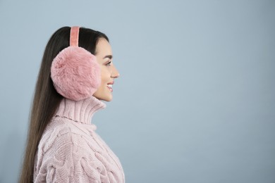 Photo of Beautiful young woman wearing earmuffs on light grey background. Space for text