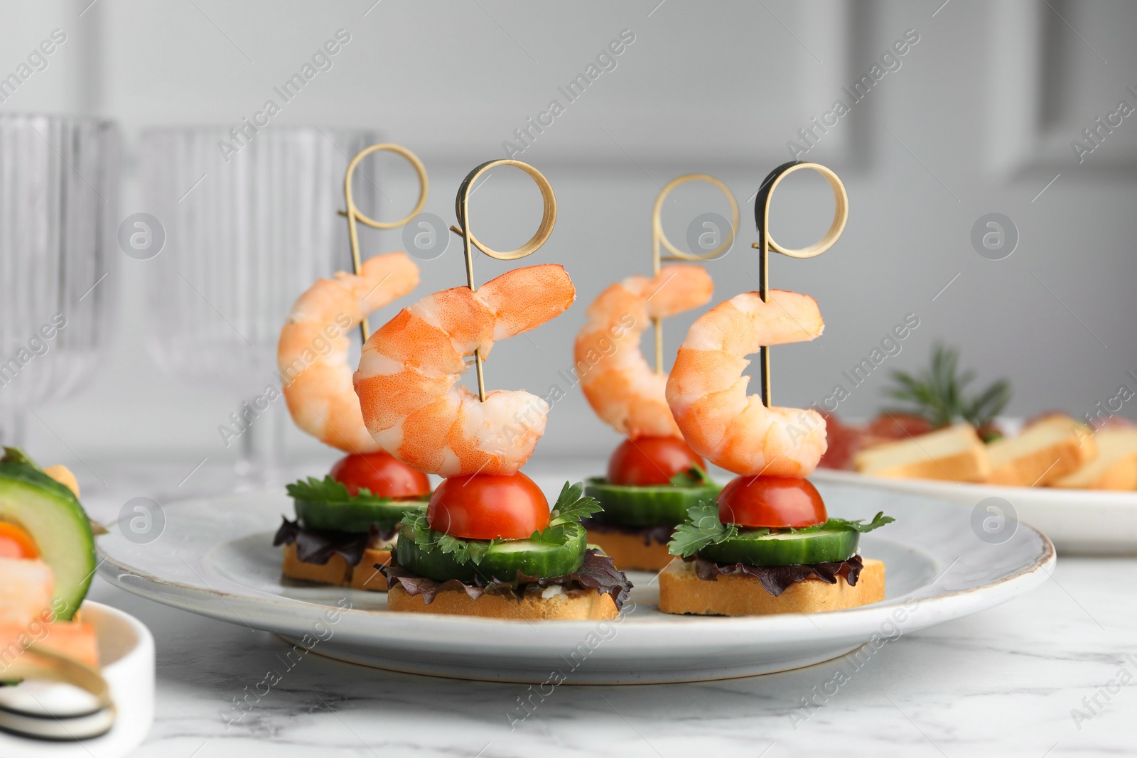 Photo of Tasty canapes with shrimps, cucumber, greens and tomatoes on white marble table