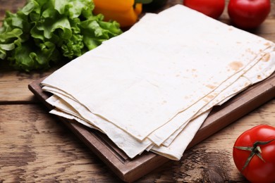 Photo of Delicious Armenian lavash and fresh vegetables on wooden table, closeup