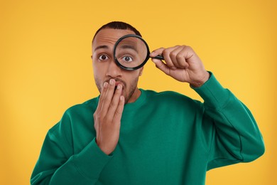 Photo of Surprised man looking through magnifier glass on orange background