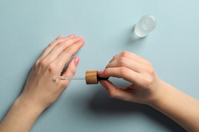 Woman dripping serum from pipette on her hand at white table, top view