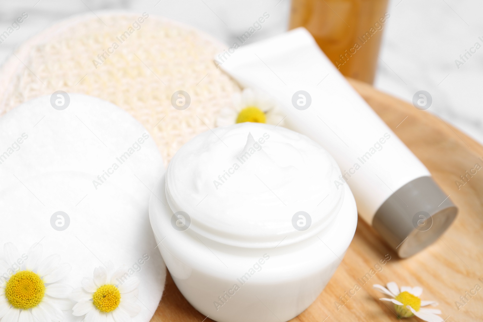 Photo of Chamomile flowers and cosmetic products on wooden plate, closeup