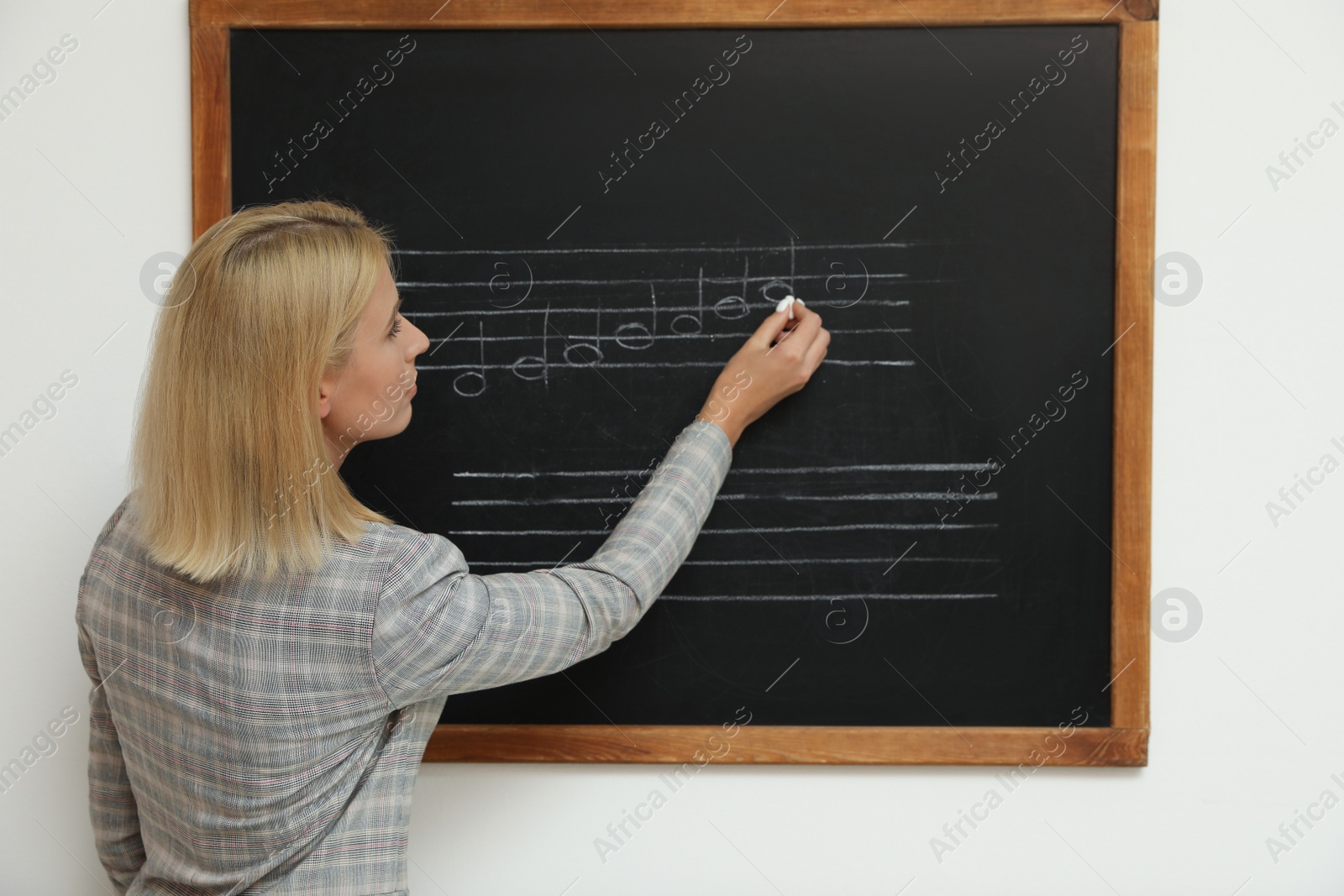 Photo of Teacher writing music notes with chalk on blackboard in classroom