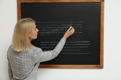 Teacher writing music notes with chalk on blackboard in classroom