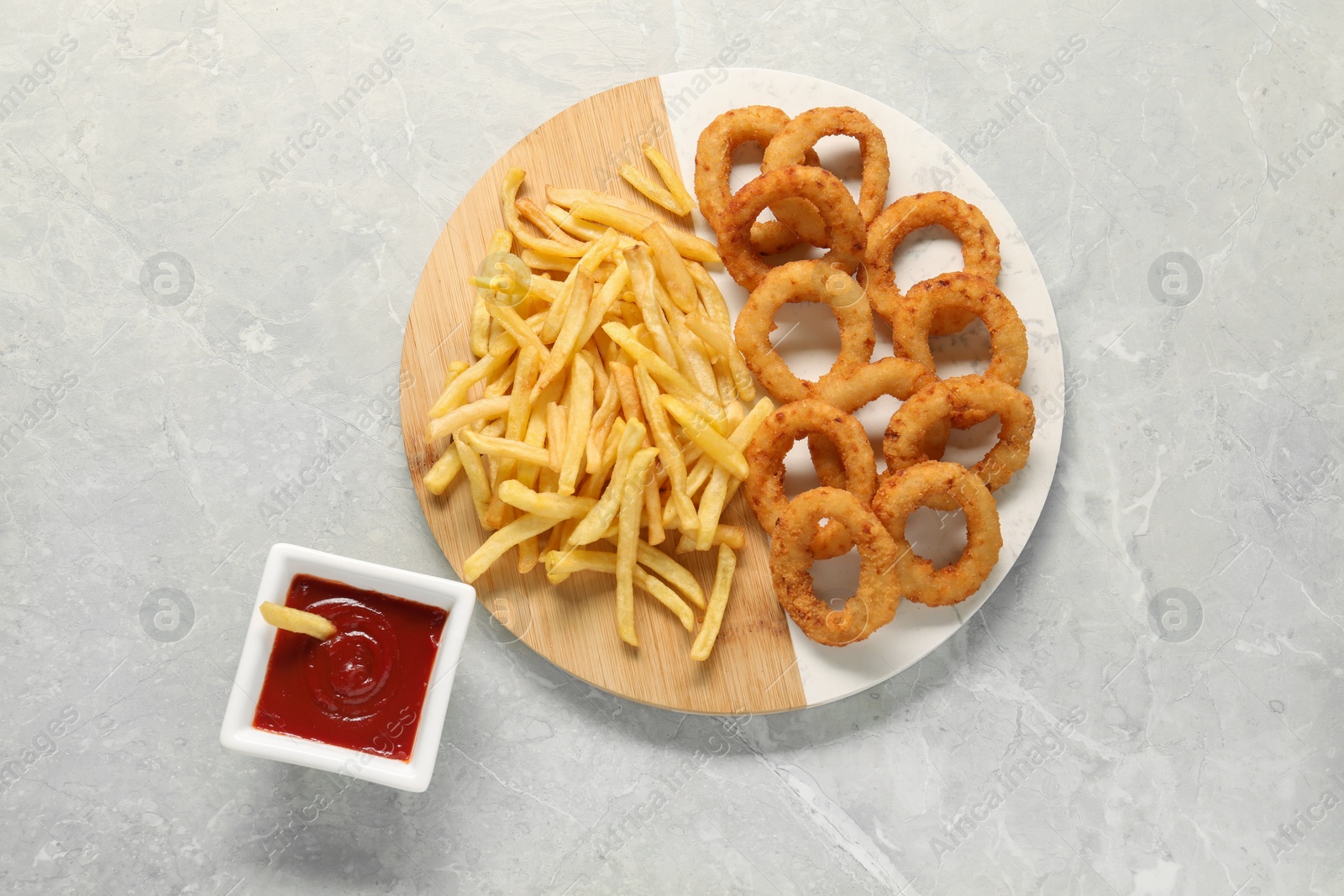 Photo of Tasty ketchup with fries and onion rings on grey marble table, flat lay