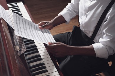 Photo of African-American man with note sheets at piano indoors, closeup. Talented musician