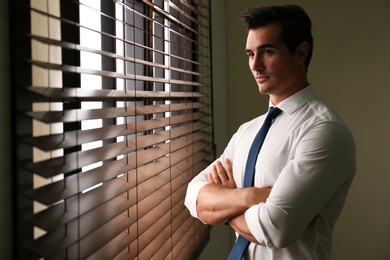 Handsome young man looking out window indoors