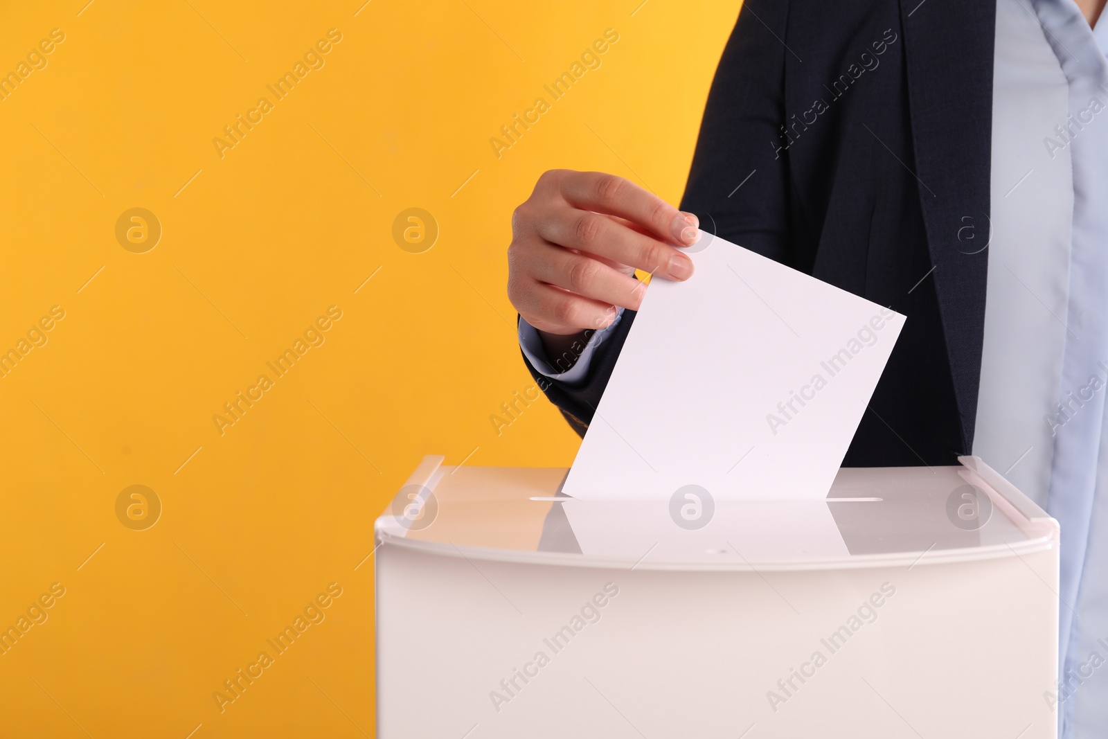 Photo of Woman putting her vote into ballot box on orange background, closeup. Space for text