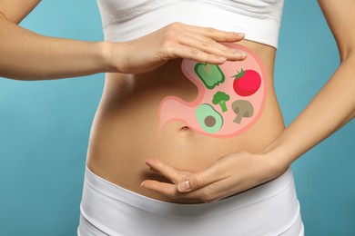 Image of Woman with image of stomach full of food drawn on her belly against light blue background, closeup. Healthy eating habits