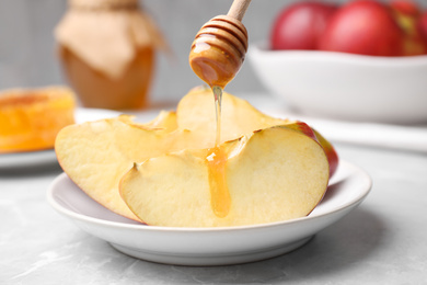 Photo of Pouring liquid honey onto apple slices from wooden dipper on light grey marble table, closeup. Rosh Hashanah holiday