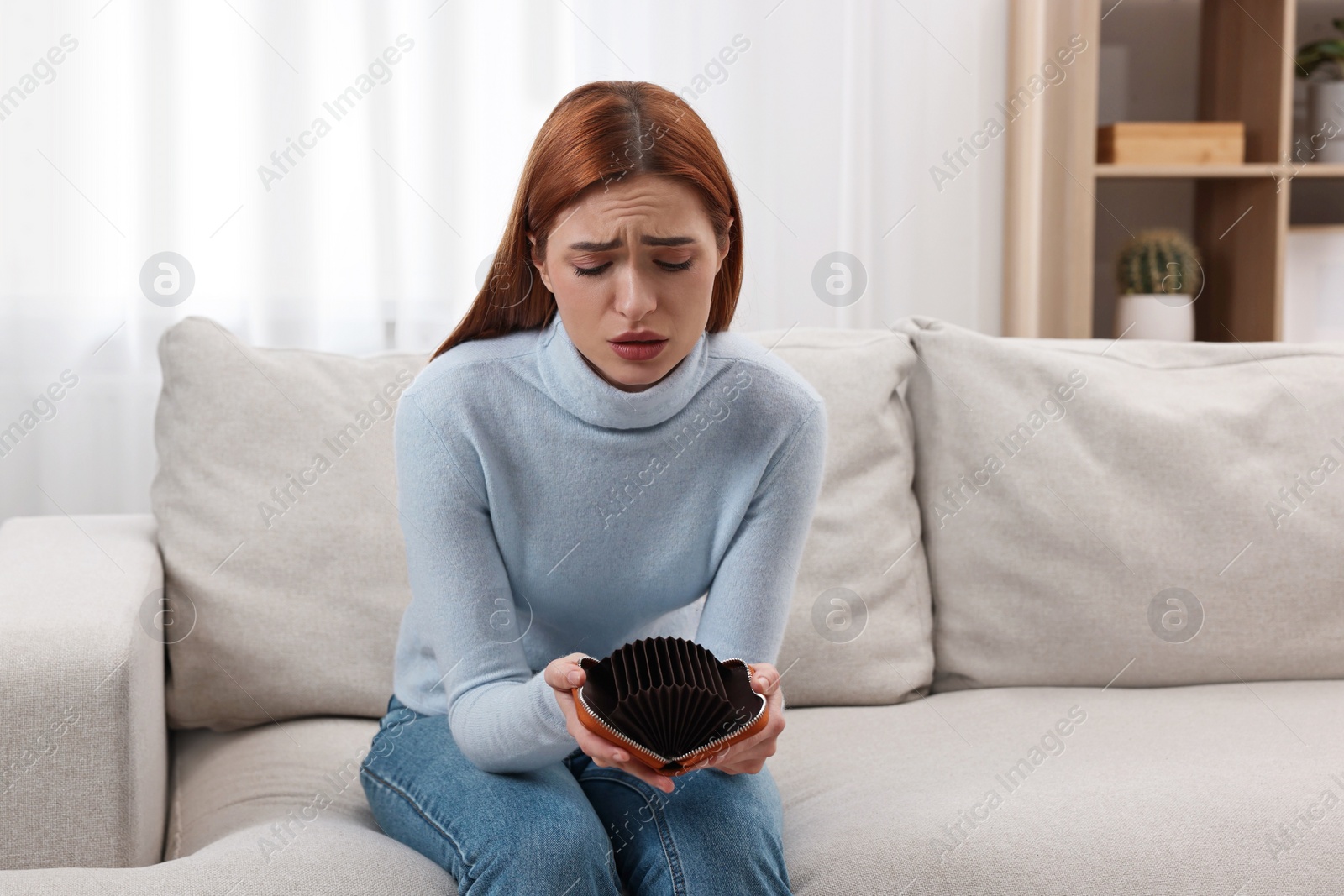 Photo of Upset woman with empty wallet on sofa indoors