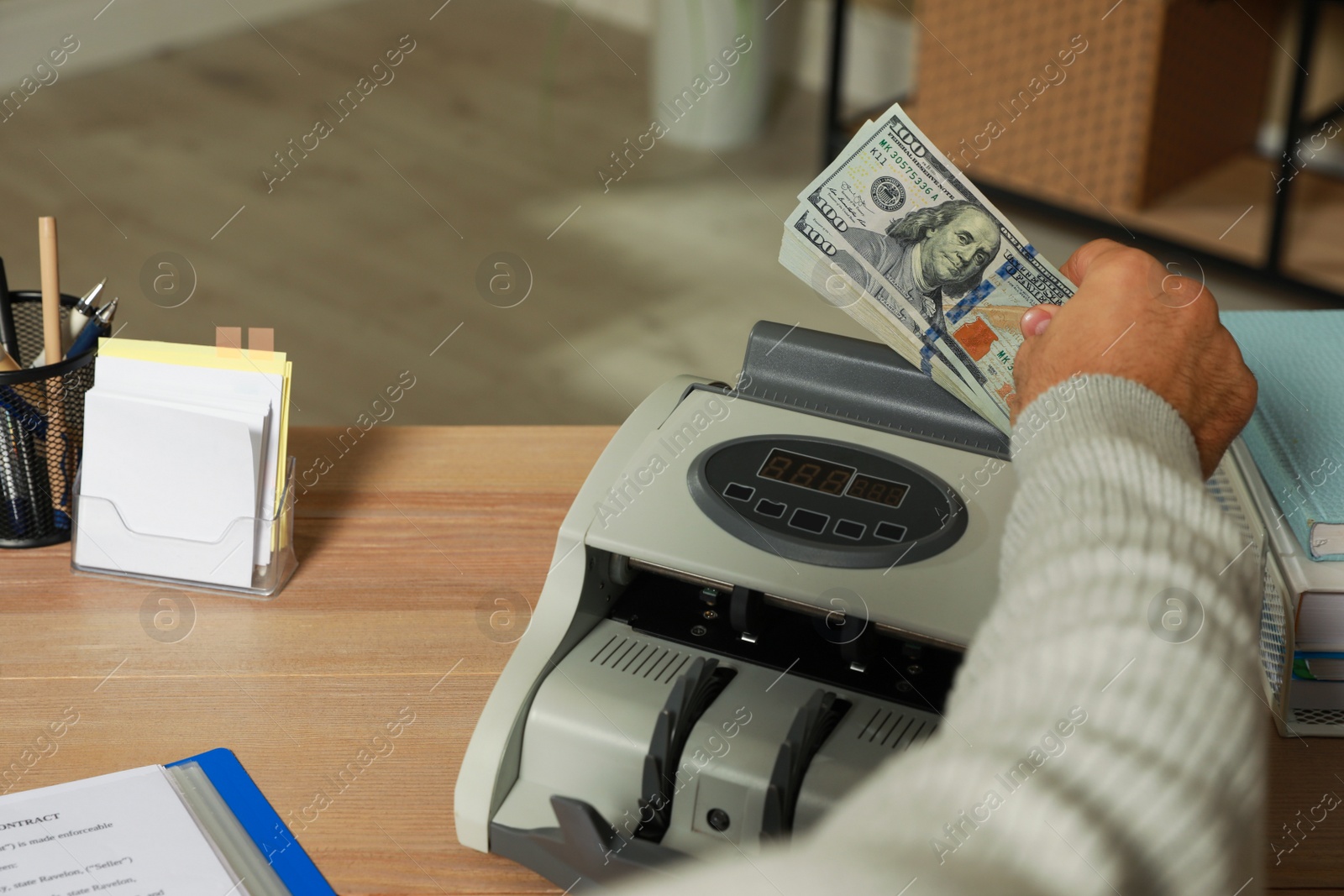 Photo of Man putting money into banknote counter at wooden table indoors, closeup