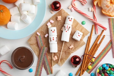 Flat lay composition with funny snowmen made of marshmallows on white wooden table
