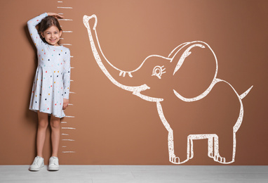 Image of Little girl measuring height and drawing of elephant near brown wall