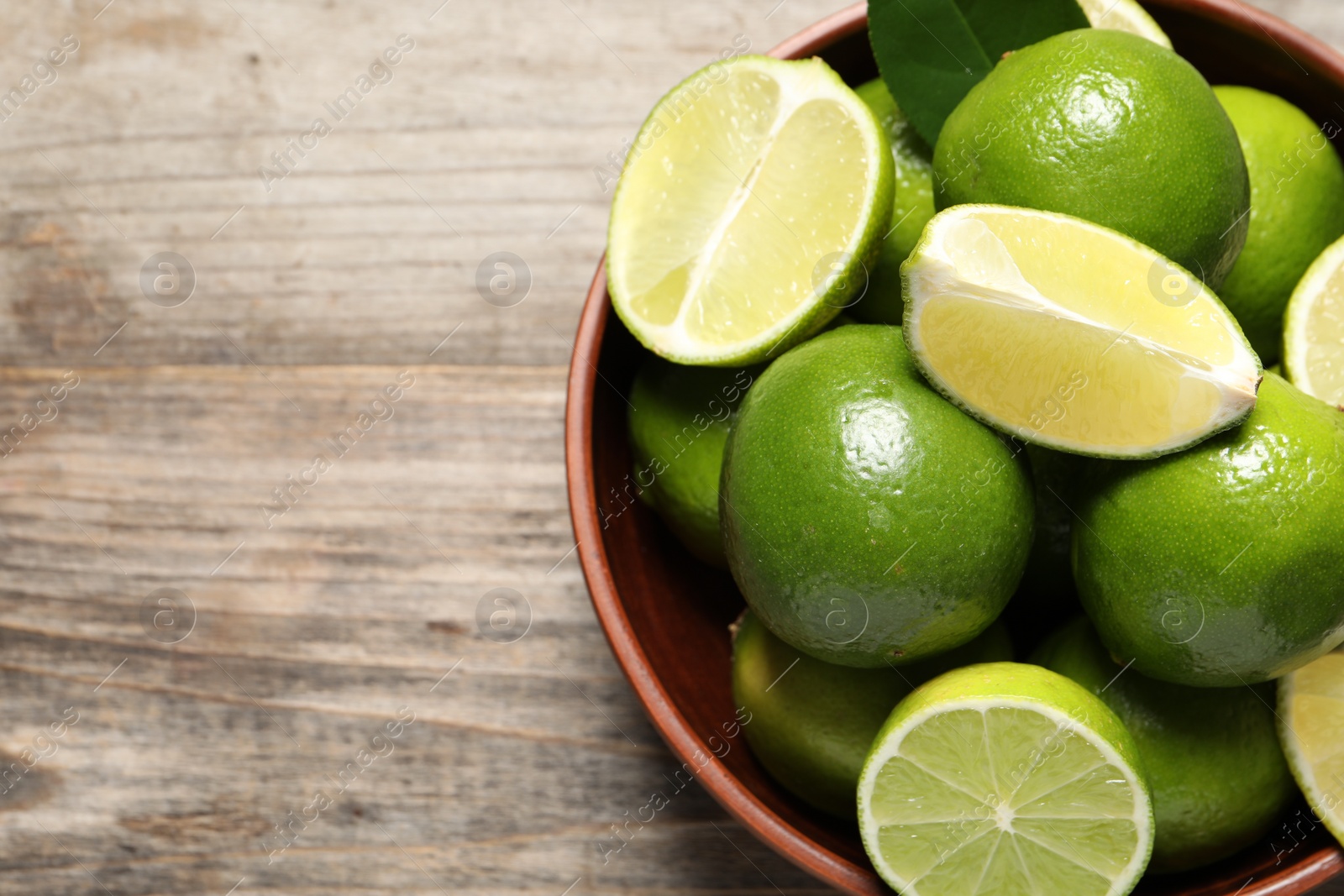 Photo of Tasty ripe limes in bowl on wooden table, top view. Space for text