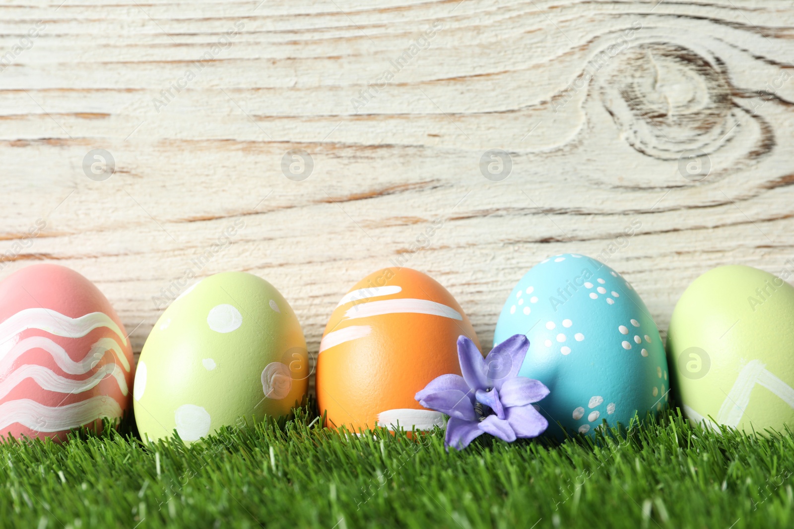 Photo of Colorful painted Easter eggs with flowers on green grass against wooden background, space for text