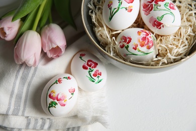 Photo of Beautifully painted Easter eggs and tulips on white table