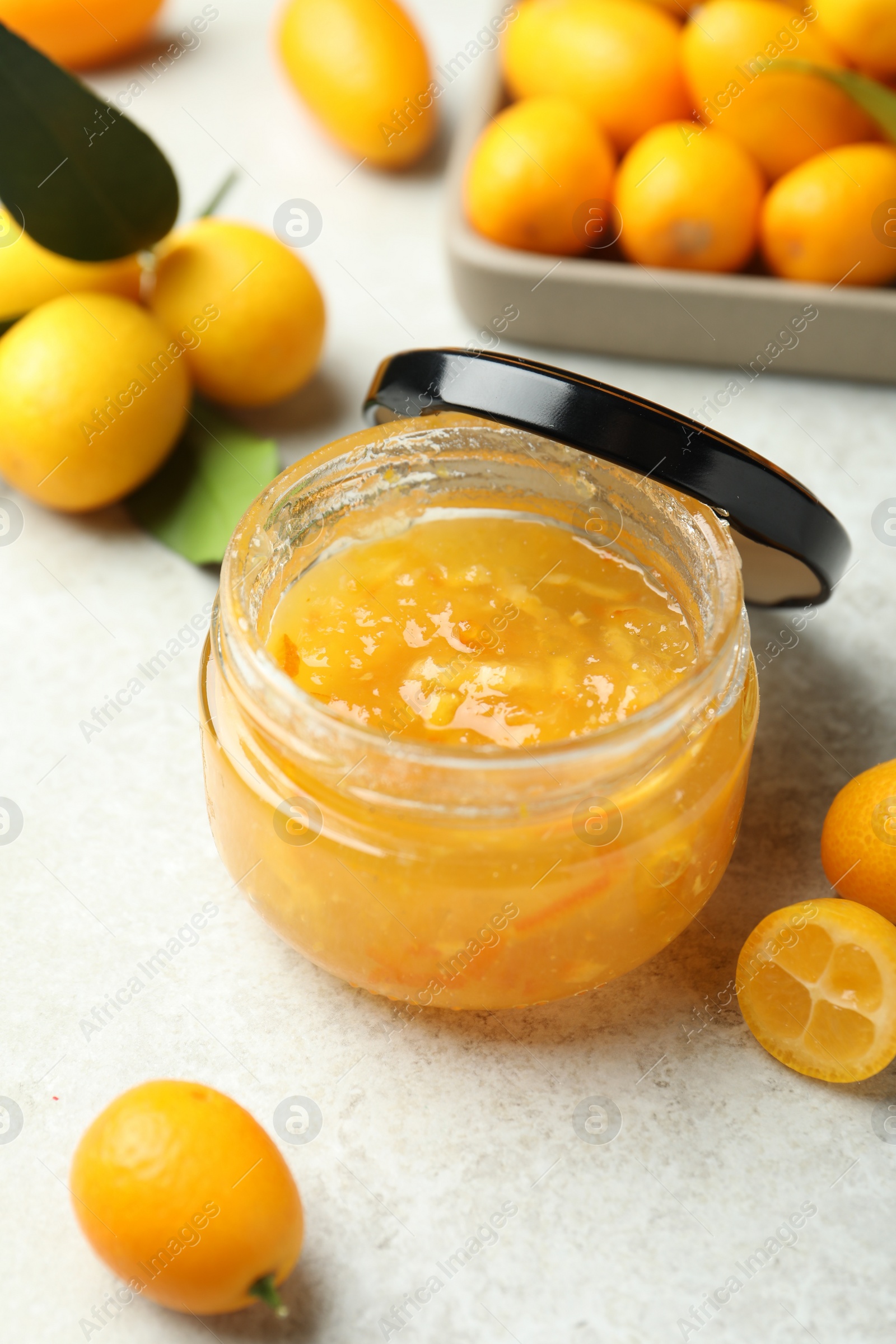 Photo of Delicious kumquat jam in jar and fresh fruits on white table