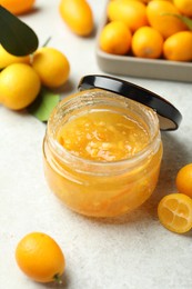 Photo of Delicious kumquat jam in jar and fresh fruits on white table