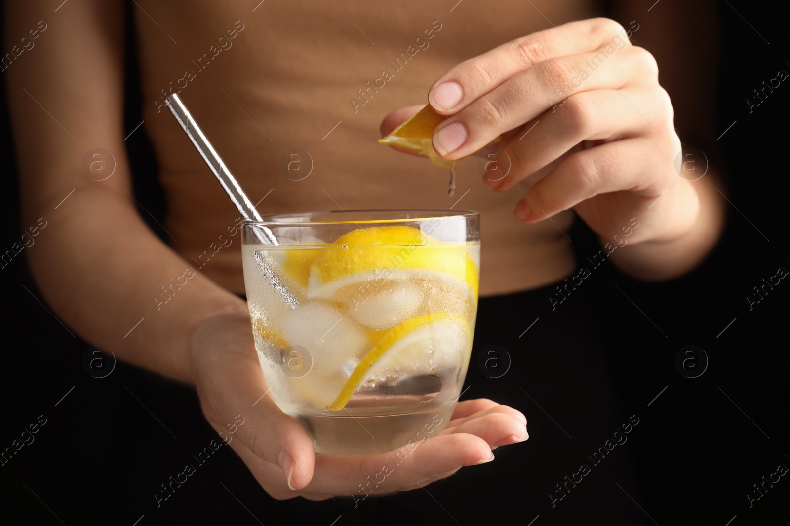 Photo of Woman squeezing lemon juice into glass of soda water with ice cubes, closeup