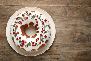 Photo of Traditional Christmas cake decorated with glaze, pomegranate seeds, cranberries and rosemary on wooden table, top view. Space for text