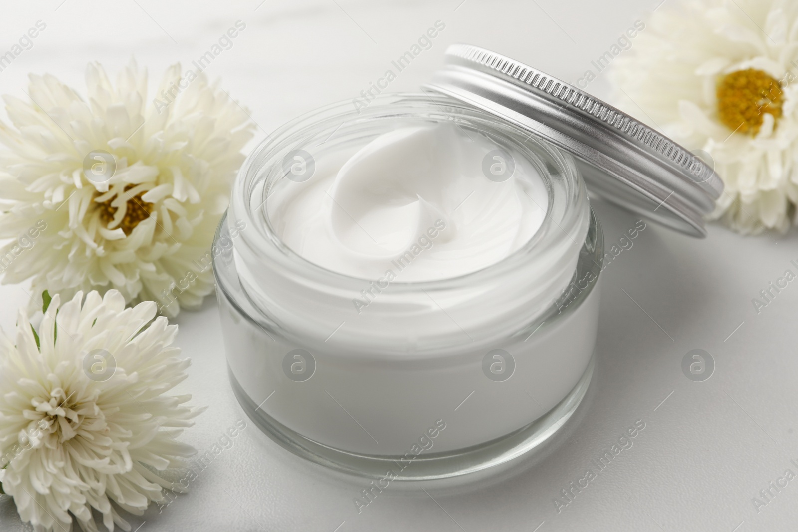Photo of Glass jar of face cream and flowers on white marble table