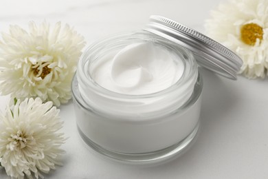 Glass jar of face cream and flowers on white marble table