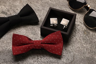 Photo of Stylish color bow ties, sunglasses and cufflinks on grey background