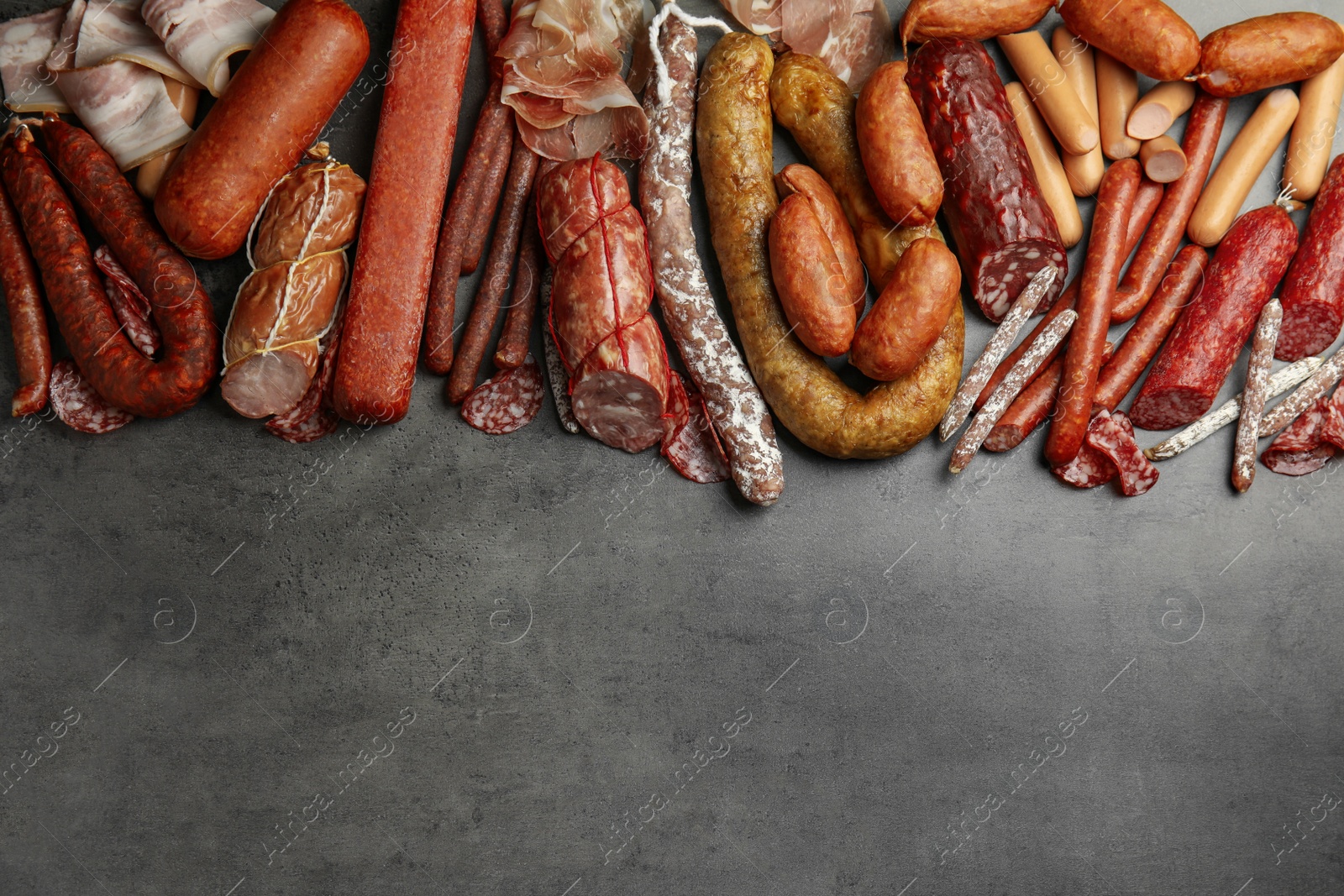 Photo of Different types of sausages on grey background, flat lay. Space for text