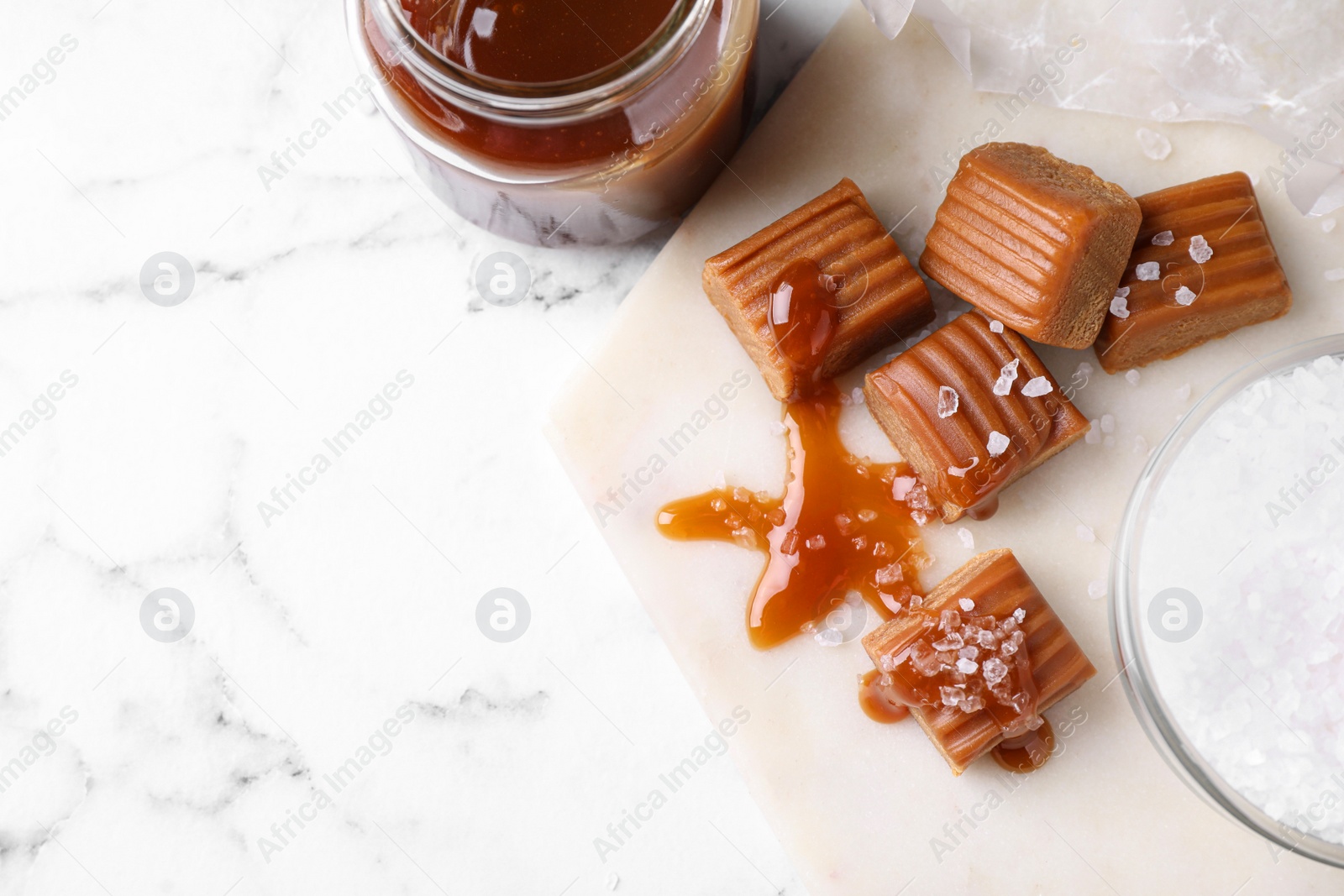 Photo of Salted caramel with sauce on marble table, flat lay. Space for text
