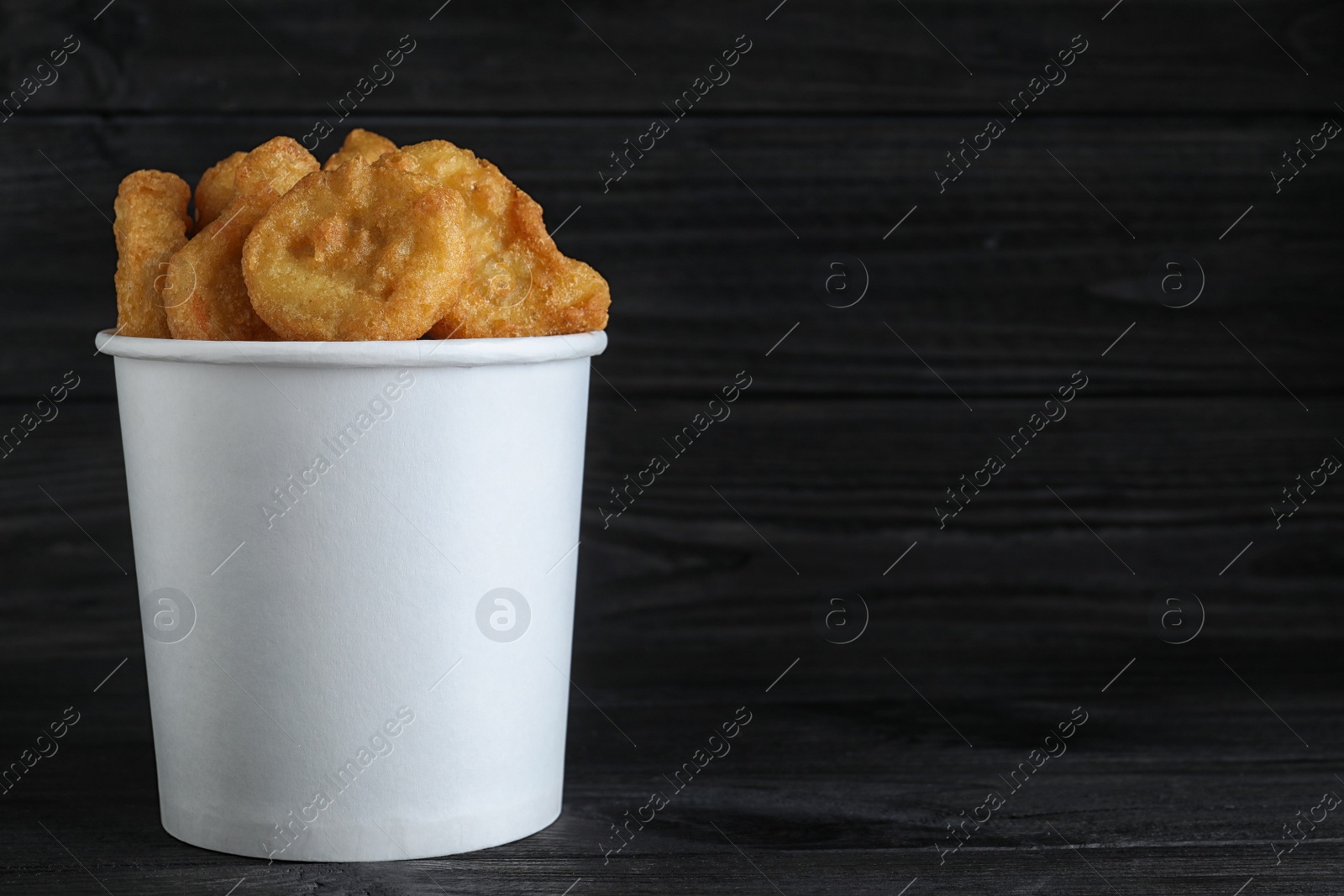 Photo of Bucket with tasty chicken nuggets on black wooden table. Space for text