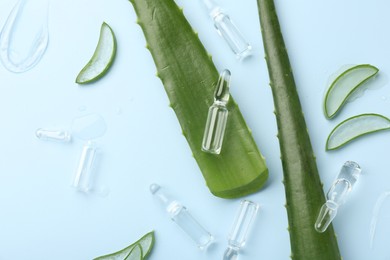 Flat lay composition with skincare ampoules and aloe leaves on light blue background