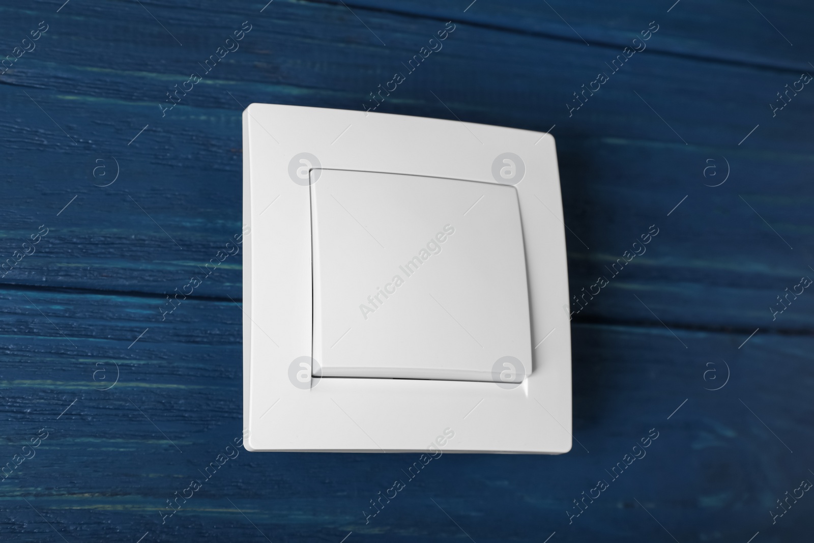 Photo of White light switch on blue wooden background, closeup