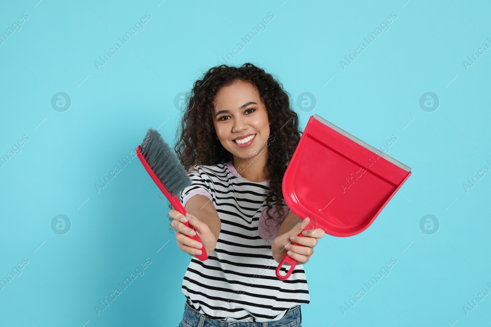 Photo of African American woman with broom and dustpan on light blue background