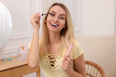 Beautiful happy woman applying mascara at home