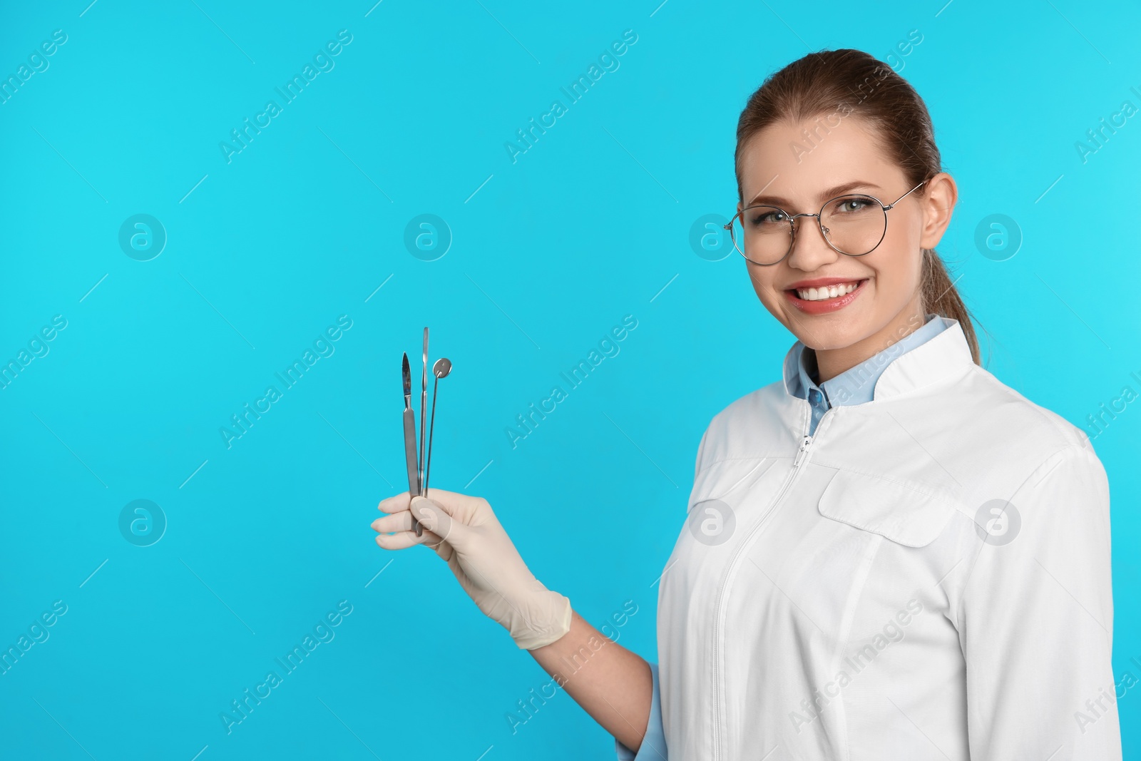 Photo of Female dentist holding professional tools on color background. Space for text