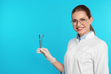 Photo of Female dentist holding professional tools on color background. Space for text