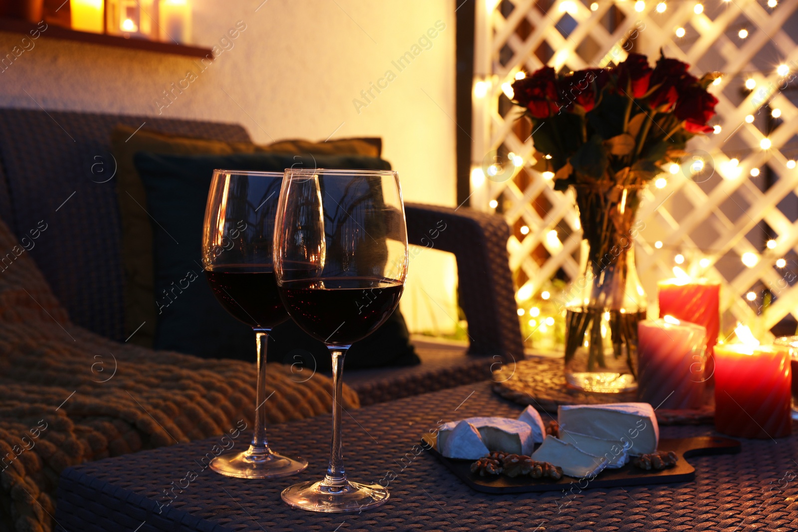 Photo of Glasses of wine, vase with roses, burning candles and snacks on outdoor terrace in evening