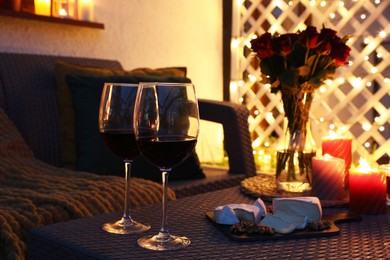 Glasses of wine, vase with roses, burning candles and snacks on outdoor terrace in evening