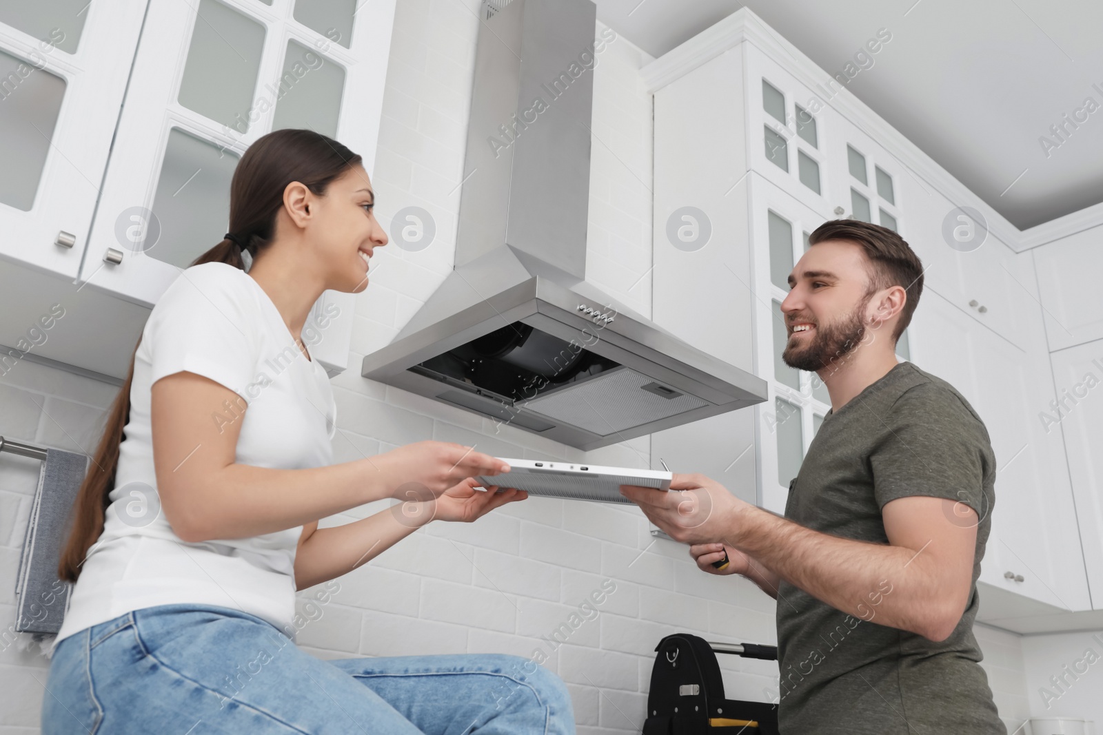 Photo of Woman giving filter of cooker hood to man in kitchen