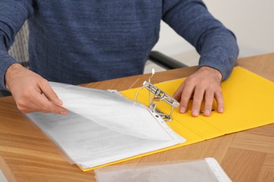Businessman putting document into file folder at wooden table in office, closeup